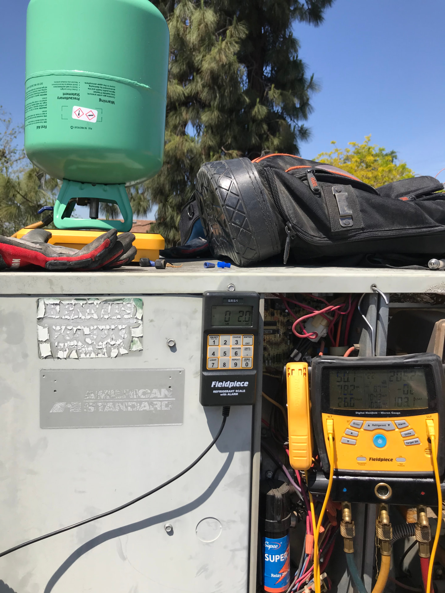 Refrigerant tank on a scale next to an American Standard condenser being charged