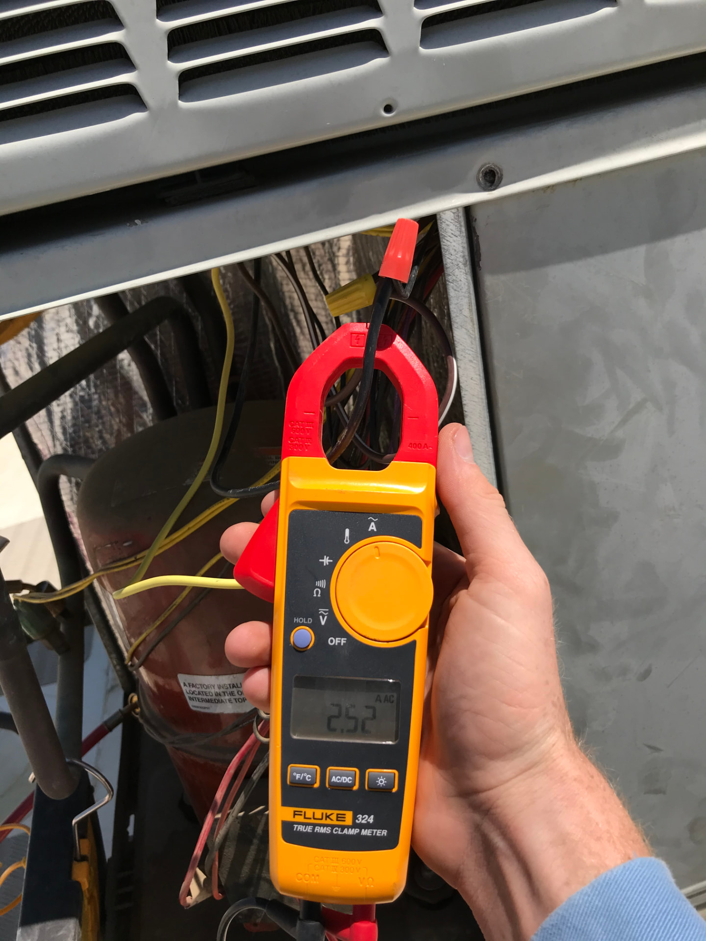 Technician using a Fluke clamp meter to test amperage inside a condenser